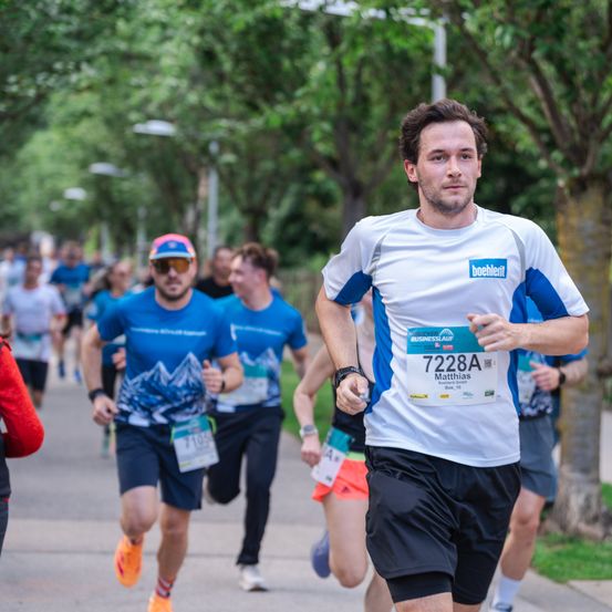Eine Gruppe von Läufern nimmt an einem Marathon bei sonnigem Wetter teil. Ein Mann in einem weißen Shirt läuft vorne.