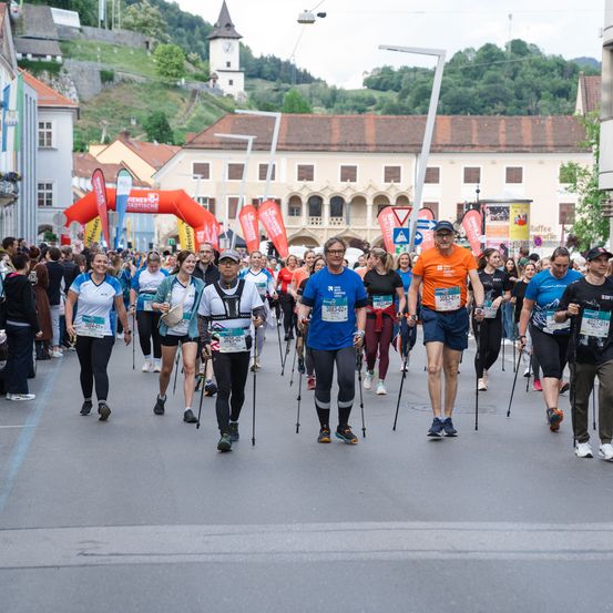 Eine große Gruppe von Menschen nimmt an einem Marathon teil, läuft mit Stöcken auf einer Stadtstraße und hat Gebäude im Hintergrund.