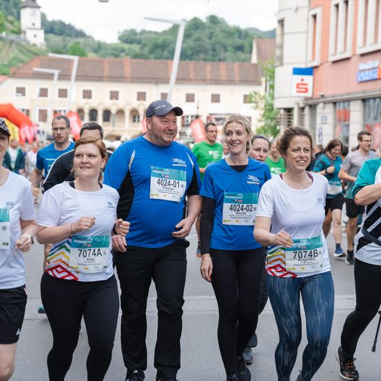 Läufer nehmen an einem Marathon teil, wobei ein Mann und Frauen gemeinsam laufen. Der Mann trägt ein blaues Shirt mit der Nummer 4024-01, während die Frauen Nummern 7074A, 4024-02 und 7074B tragen.