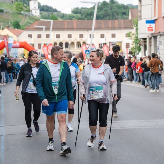 Marathon-Teilnehmer auf der Straße mit Nummern auf ihren Trikots, umgeben von Zuschauern, Gebäuden und Grünanlagen.