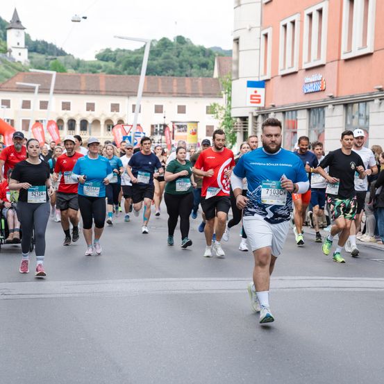 Ein Marathon mit mehreren Läufern auf einer Stadtstraße mit Gebäuden an der Seite. Ein Läufer trägt ein blaues Shirt und weiße Shorts.