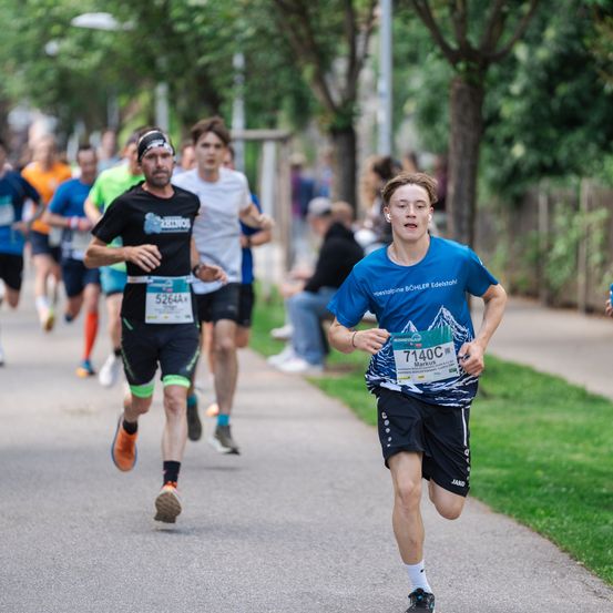 Teilnehmer eines Marathons, ein Läufer trägt ein blaues Shirt mit der Nummer 7140, ein anderer ein schwarzes Shirt mit Rhino-Logo. Beide konzentrieren sich auf den Lauf.