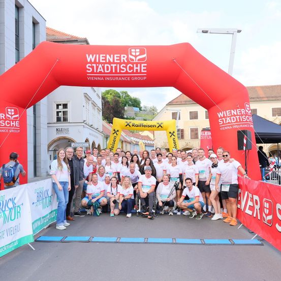 Eine Gruppe von Läufern in weißen Shirts posiert für ein Foto vor einem roten Bogen, gesponsert von Wiener Stadtische.