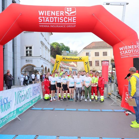 Marathonläufer stehen an der Startlinie mit einem großen roten Bogen im Hintergrund, gesponsert von Wiener Stadtische und Raiffeisen. Gebäude und eine Straße sind sichtbar.