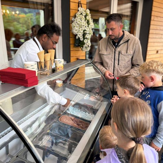 Ein Mann serviert Eis für eine Gruppe von Kindern an einem Eisstand im Freien.