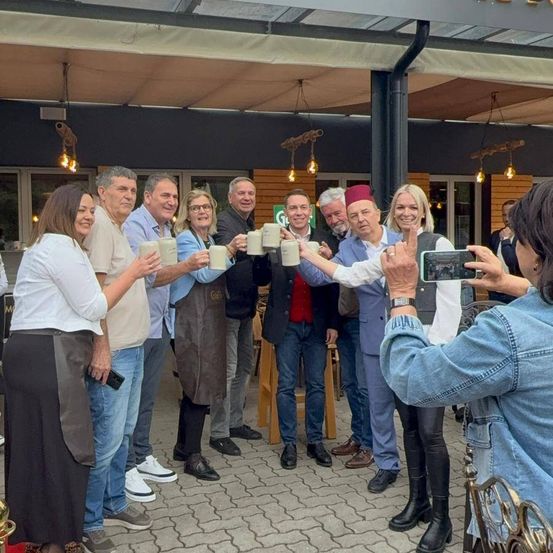 Eine Gruppe von Menschen, möglicherweise eine Familie, steht vor einem Restaurant, hält Tassen in der Hand, lächelt und posiert für ein Foto.
