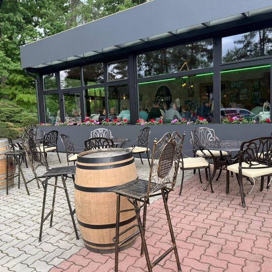 Ein Außenbereich mit Tischen und Stühlen vor einem Restaurant mit Glasfenstern und einem Blumenkasten.