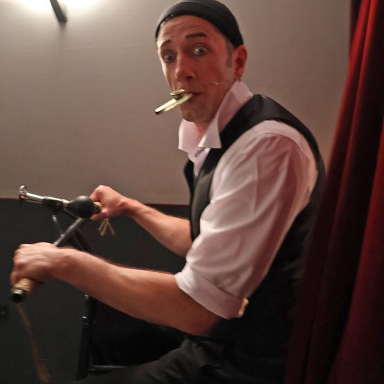 Ein Mann in schwarzem Hut und Weste spielt eine Trompete in ein Mikrofon auf einem Ständer.