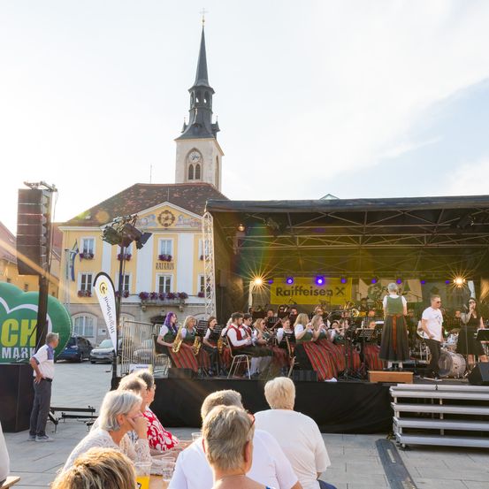Eine Band spielt auf einer Bühne vor einem Gebäude mit einem Turm im Hintergrund. Das Publikum schaut von unten zu.