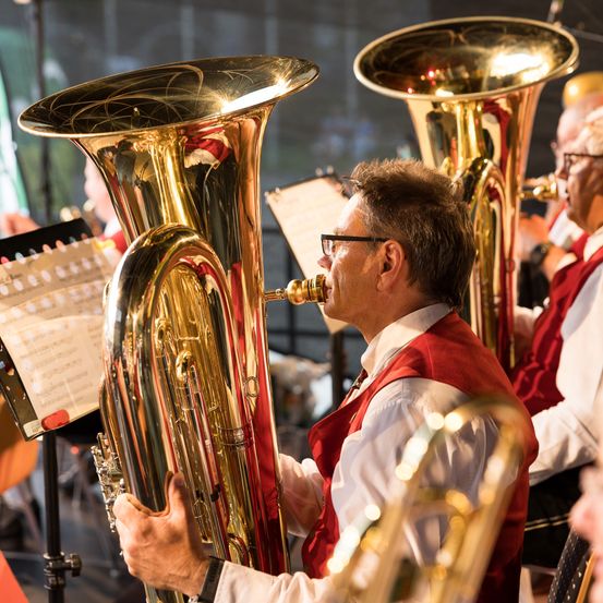 Ein Mann spielt eine goldene Tuba, während er neben anderen in einem Konzert steht, mit einem Musikblatt in der Nähe.