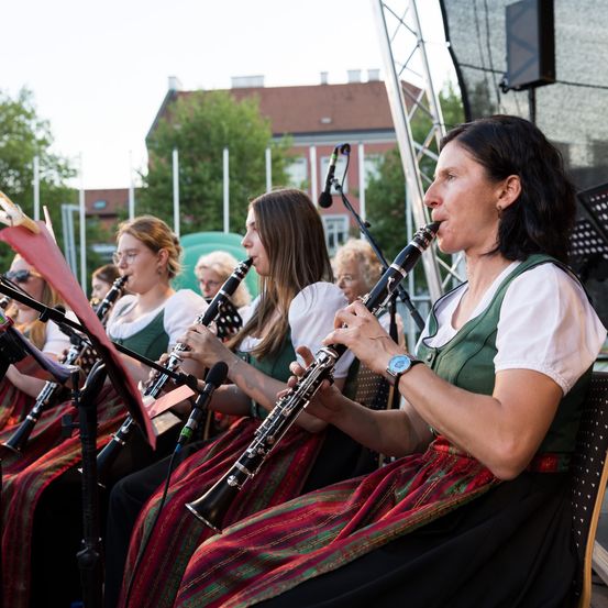 Eine Gruppe von Musikern spielt Klarinetten auf der Bühne. Sie sind in traditioneller Kleidung gekleidet. Die Umgebung ist im Freien.