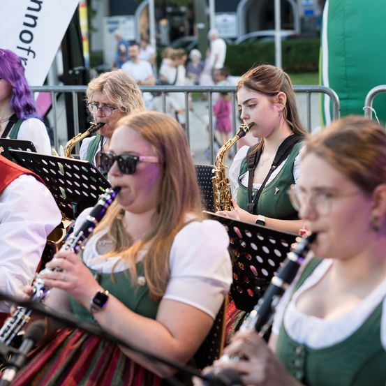 Eine Gruppe von Musikern in traditioneller grüner und weißer Kleidung spielt im Freien mit Saxophonen und Klarinetten vor Publikum.