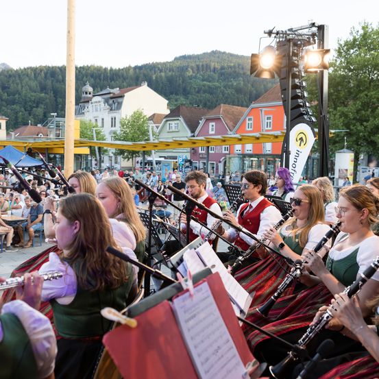 Eine Gruppe von Musikern spielt auf der Bühne mit Flöten und Klarinetten vor einem Publikum auf einem Stadtplatz.