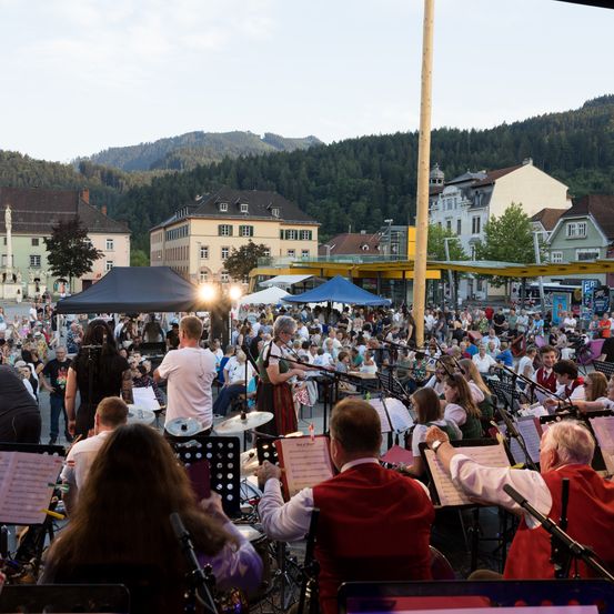 Ein großes Open-Air-Konzert mit einer Band auf der Bühne, umgeben von einem Publikum unter einem Zelt, mit Bergen im Hintergrund.