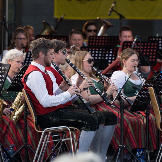 Eine Band spielt auf der Bühne, mit Musikern, die Klarinetten, Saxophone und Trompeten spielen. Das Publikum beobachtet von vorne.