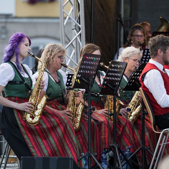 Eine Gruppe von Frauen und Männern in traditioneller Kleidung spielt Saxophon auf der Bühne mit Notenständern.