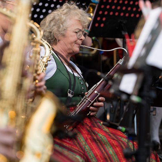 Eine ältere Frau mit Brille spielt im Musikverein ein Fagott und lächelt. Sie trägt ein grün-rotes Kostüm.