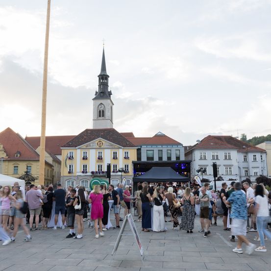Ein überfüllter Stadtplatz mit einer Kirche, Zelten und einer Bühne, gefüllt mit lässig gekleideten Menschen.