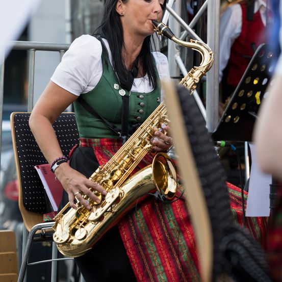 Eine Frau in traditioneller Kleidung spielt auf einer Konzertsitzbank eine Saxophon.