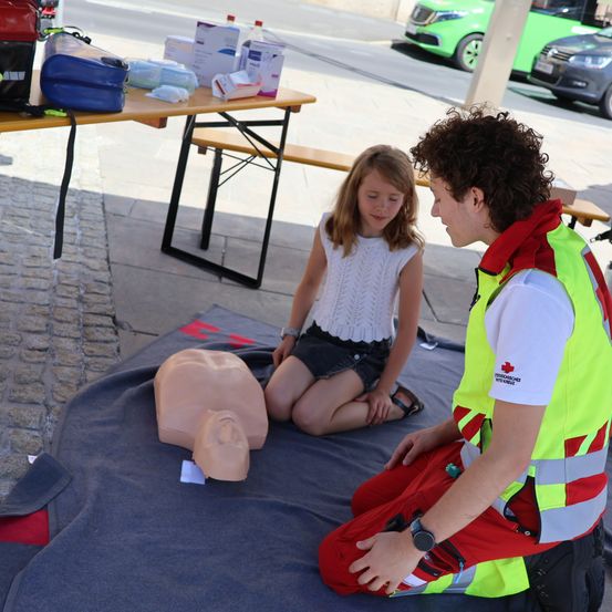 Ein junger Mann in einer Sicherheitsweste demonstriert einer jungen Frau auf einer Decke CPR an einem Mannequin.