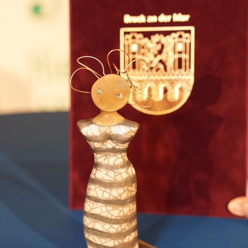 Eine Figur mit einem rissigen Muster steht vor einem roten Hintergrund mit einem Logo. Die Figur hat einen runden Kopf und einen Körper mit einer rissigen Textur.