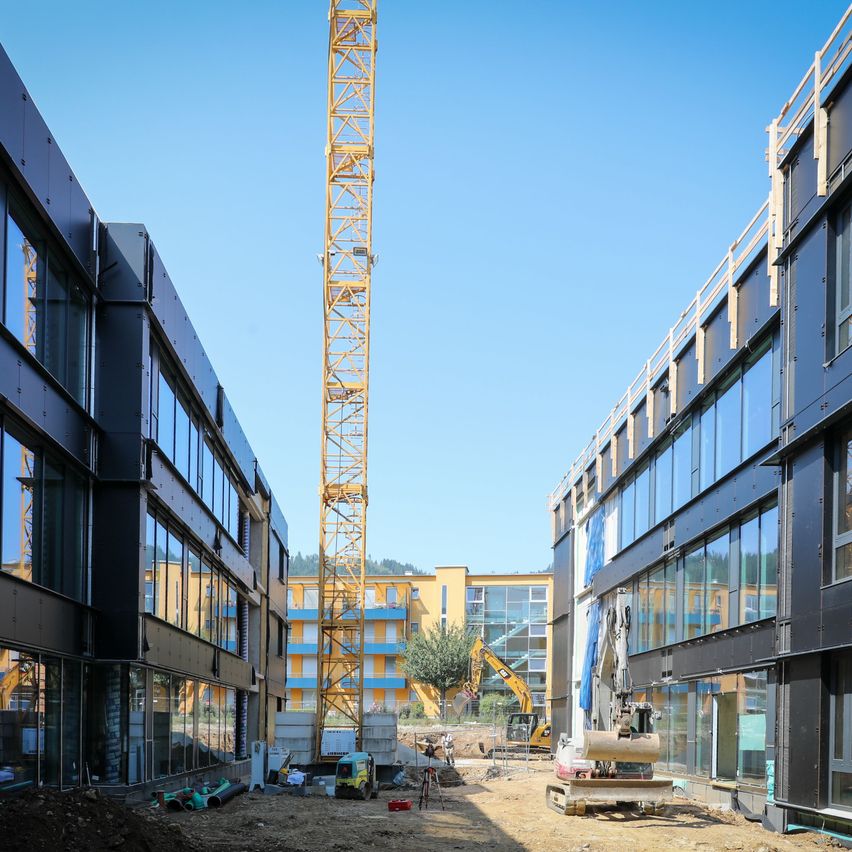 Eine Baustelle mit einem hohen gelben Kran und zwei teilweise fertiggestellten Gebäuden unter einem klaren blauen Himmel.