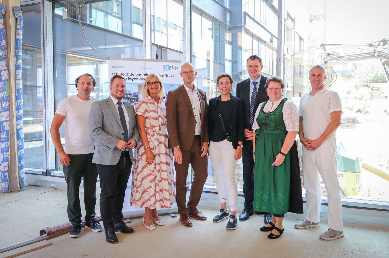 Eine Gruppe von Menschen, möglicherweise Fachleute, steht in einem modernen Gebäude und lächelt für ein Foto. Sie sind in formeller Kleidung gekleidet.