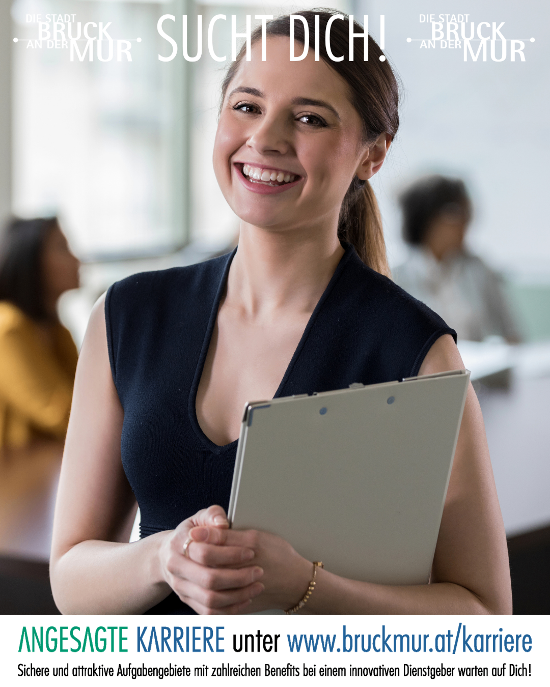 Eine lächelnde Frau in einem schwarzen ärmellosen Oberteil hält eine Clipboard in einer professionellen Umgebung, mit anderen Personen im Hintergrund.