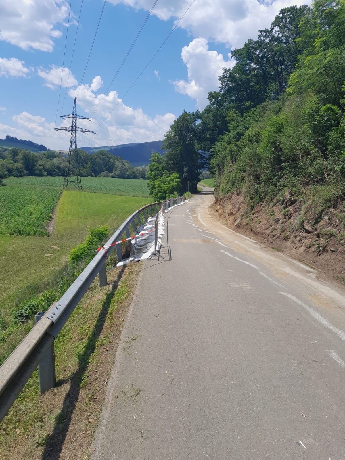 Eine leere Straße mit einem Metallgeländer. Die Straße hat eine Baustellensperre. Hinter der Sperre befindet sich ein Feld und ein Stromleitungsmast.