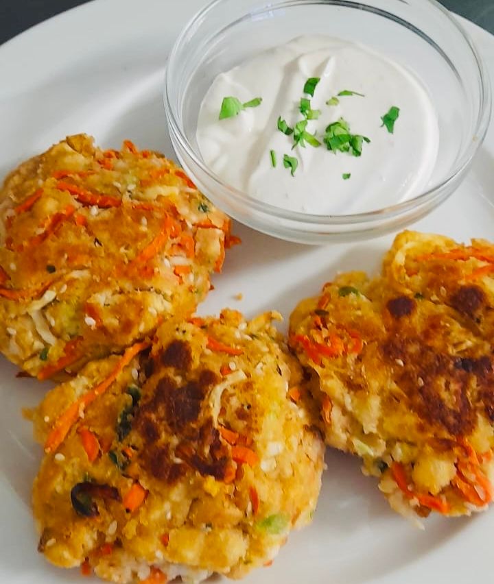 Drei goldbraune Patties mit einer leicht knusprigen Außenseite und einer cremigen Dip in einer weißen Schüssel mit grünen Kräutern obenauf.