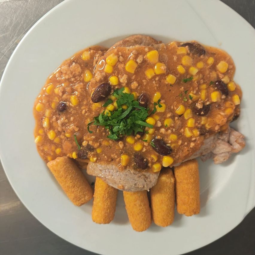 Ein Teller mit Fleisch, überzogen mit einer cremigen Sauce, Mais, schwarzen Bohnen und mit Petersilie garniert auf einem weißen Teller.