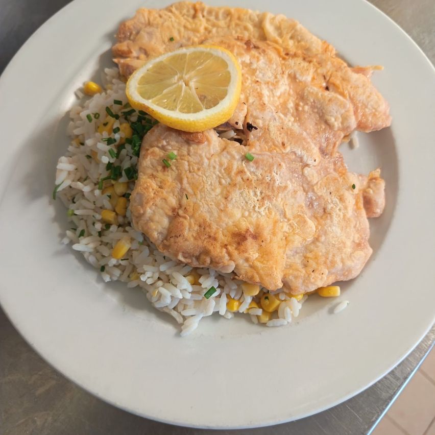 Ein Teller mit gebratenen Fischfilets, Reis, Mais und einer Zitronenscheibe obenauf.