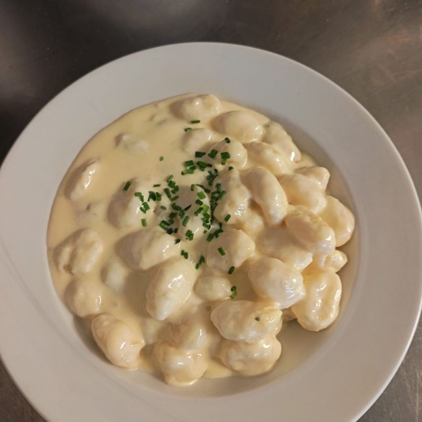Ein weißer Teller mit cremigen Gnocchi, überzogen mit gehackten Schnittlauch, auf einer metallischen Oberfläche.