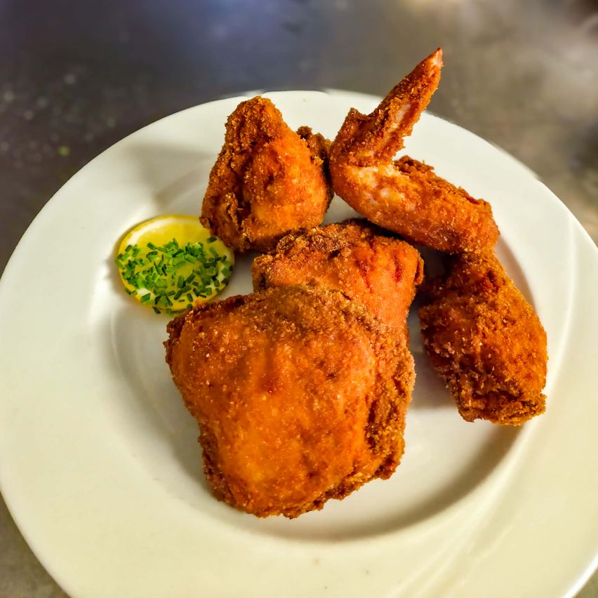 Ein weißer Teller mit gebratenen Hühnchenstücken und einer Zitronenscheibe, die mit grünen Kräutern garniert ist.