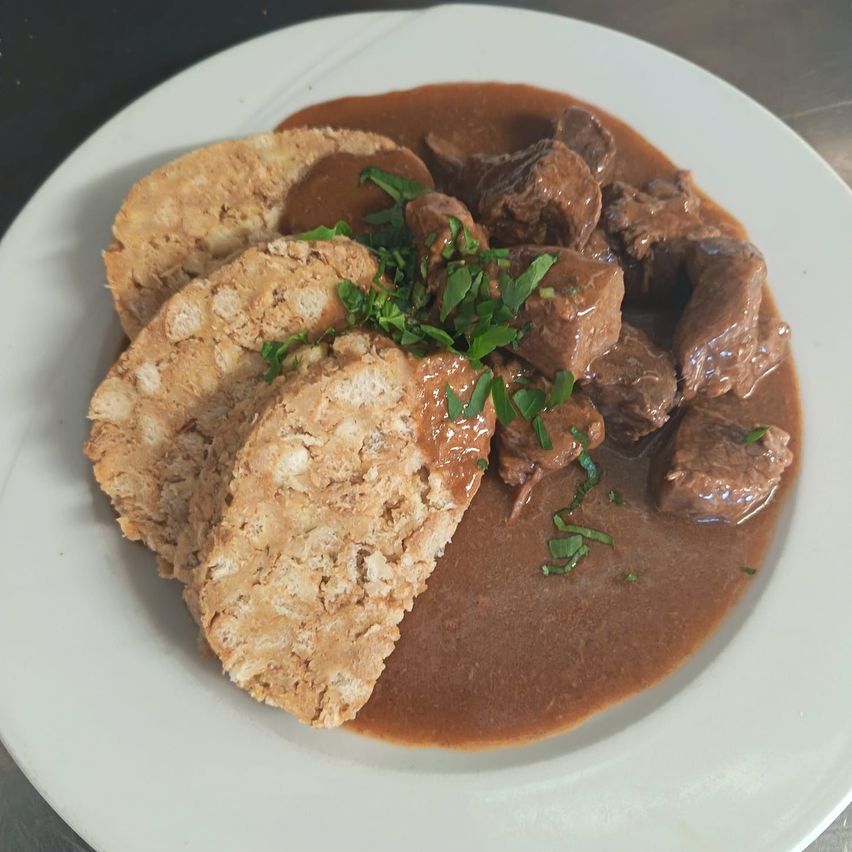 Ein Teller mit einem herzhaften Eintopf aus Fleisch und Soße, begleitet von zwei Brotscheiben.