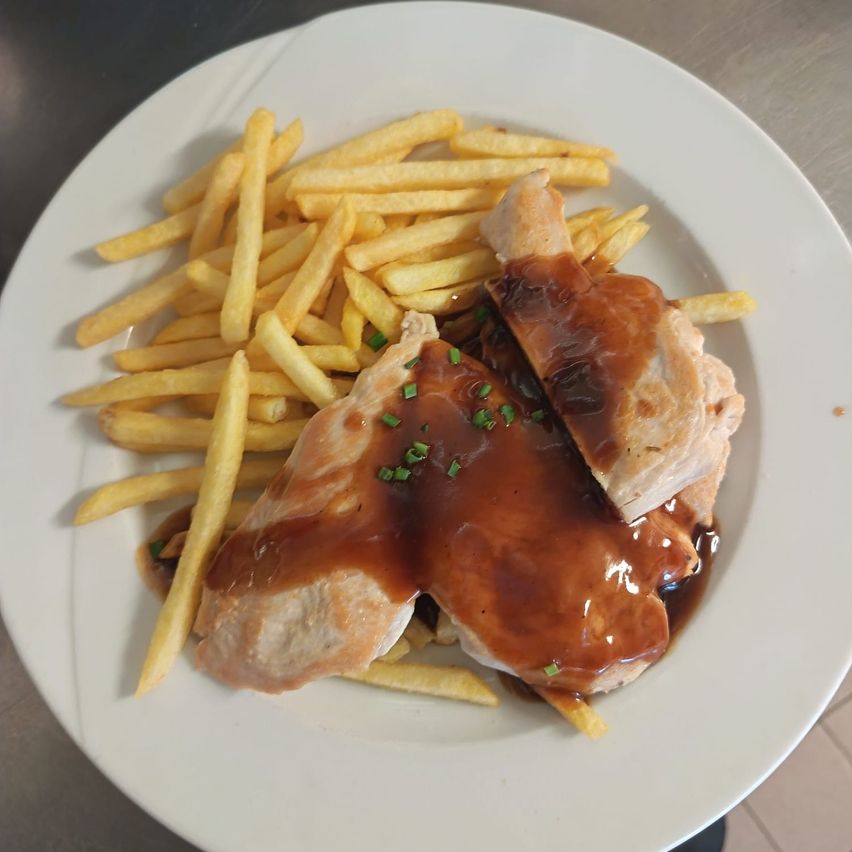 Ein weißer Teller mit Hähnchenbrust, überzogen mit Soße, und Pommes Frites auf der Seite.