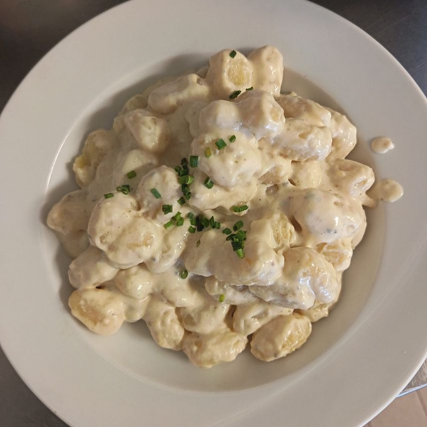 Ein weißer Teller mit cremigen Gnocchi, garniert mit gehackten Frühlingszwiebeln.
