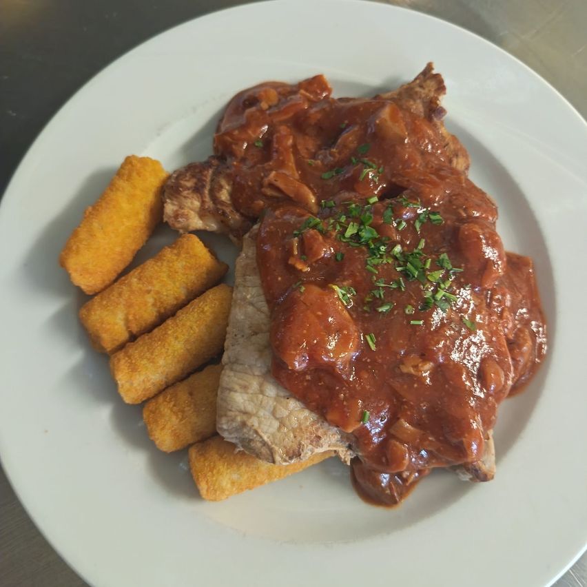 Ein Teller mit einem Fleischgericht, das mit Sauce überzogen und mit Kräutern garniert ist, begleitet von frittierten Kartoffelsticks.