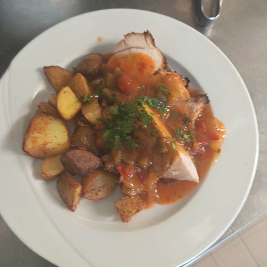 Ein Teller mit gebratenem Schweinefleisch in einer reichhaltigen Sauce, begleitet von goldbraunen gebratenen Kartoffeln und mit frischen Kräutern garniert.
