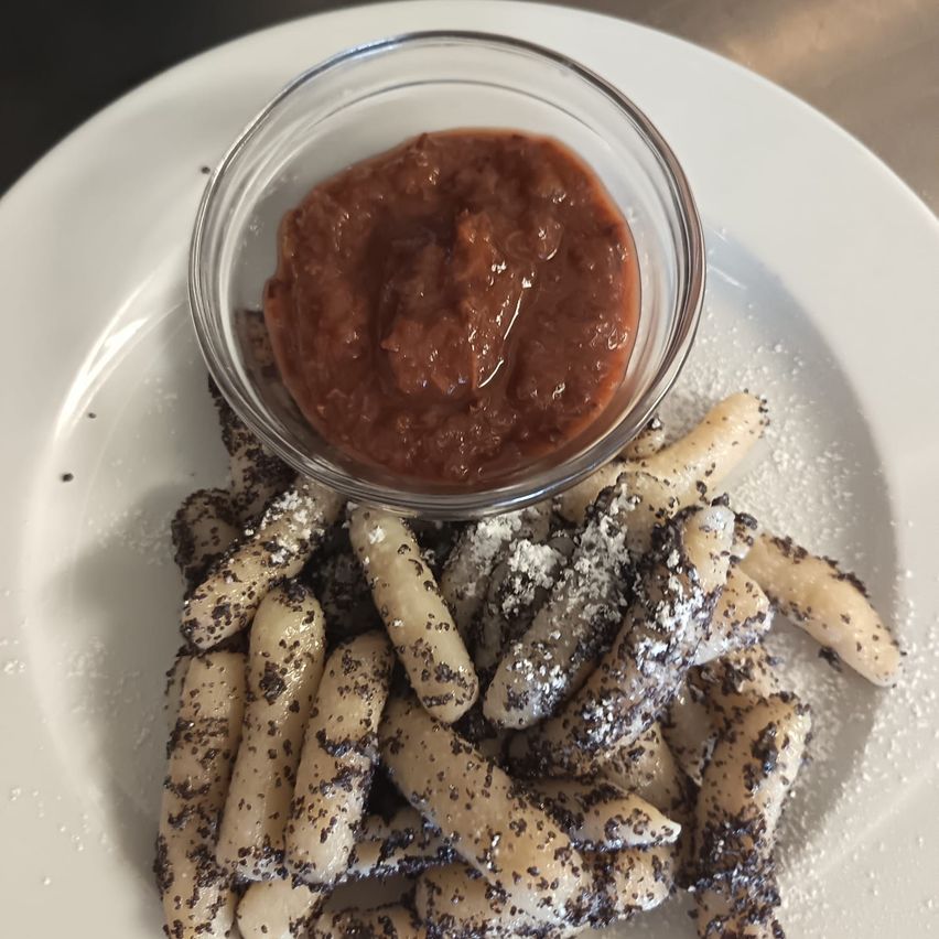 Ein weißer Teller mit einer kleinen Schüssel roter Sauce und einem Haufen Kartoffelsticks, die mit schwarzen und weißen Toppings bestreut sind.
