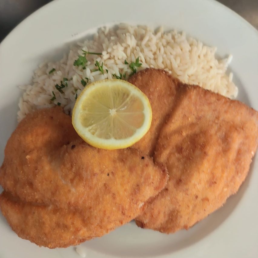 Zwei Stücke panierter gebratener Fisch mit einer Zitronenscheibe auf einem Teller mit Reis.