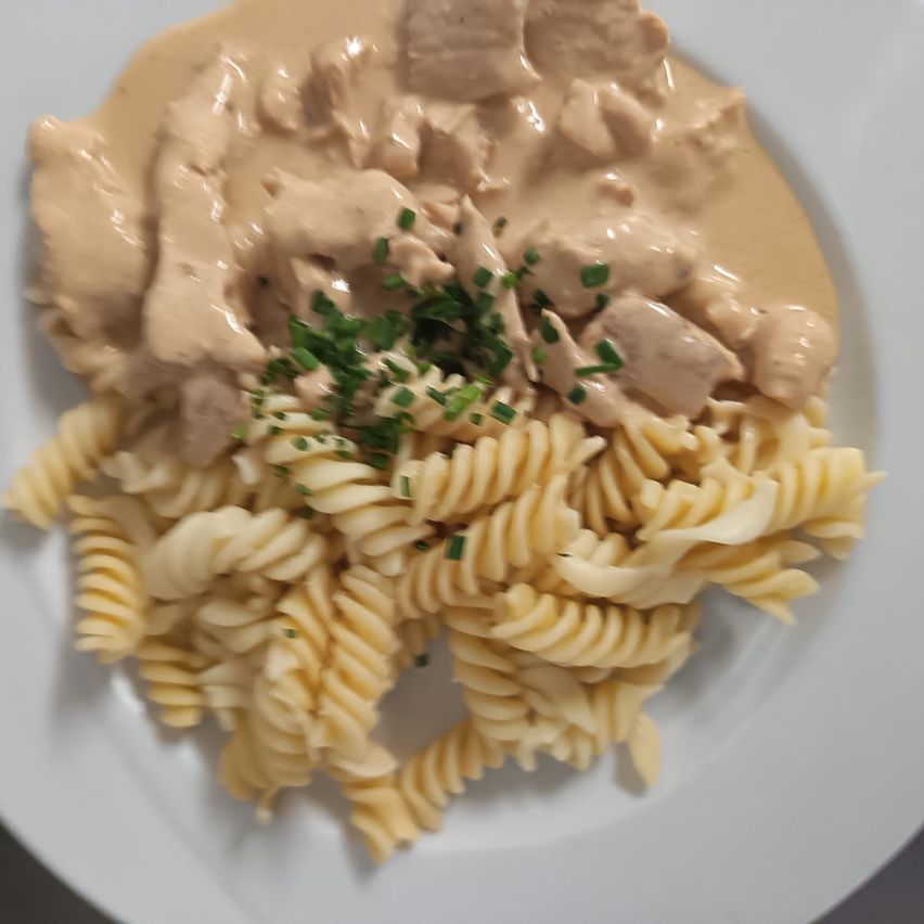 Ein Teller mit cremiger Hühnchen-Pasta in hellbrauner Sauce, garniert mit grünen Kräutern.
