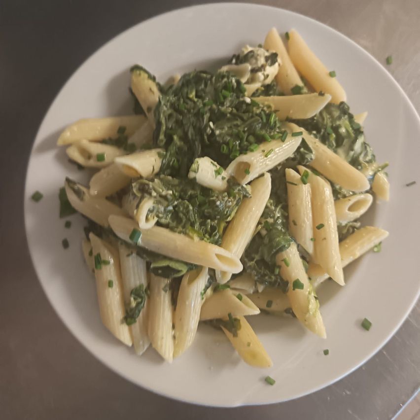 Ein Teller mit cremiger Pasta, überzogen mit Spinat und grünen Kräutern.