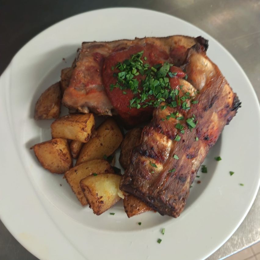 Ein weißer Teller mit gegrillten Rippchen und gebratenen Kartoffeln, garniert mit Petersilie.