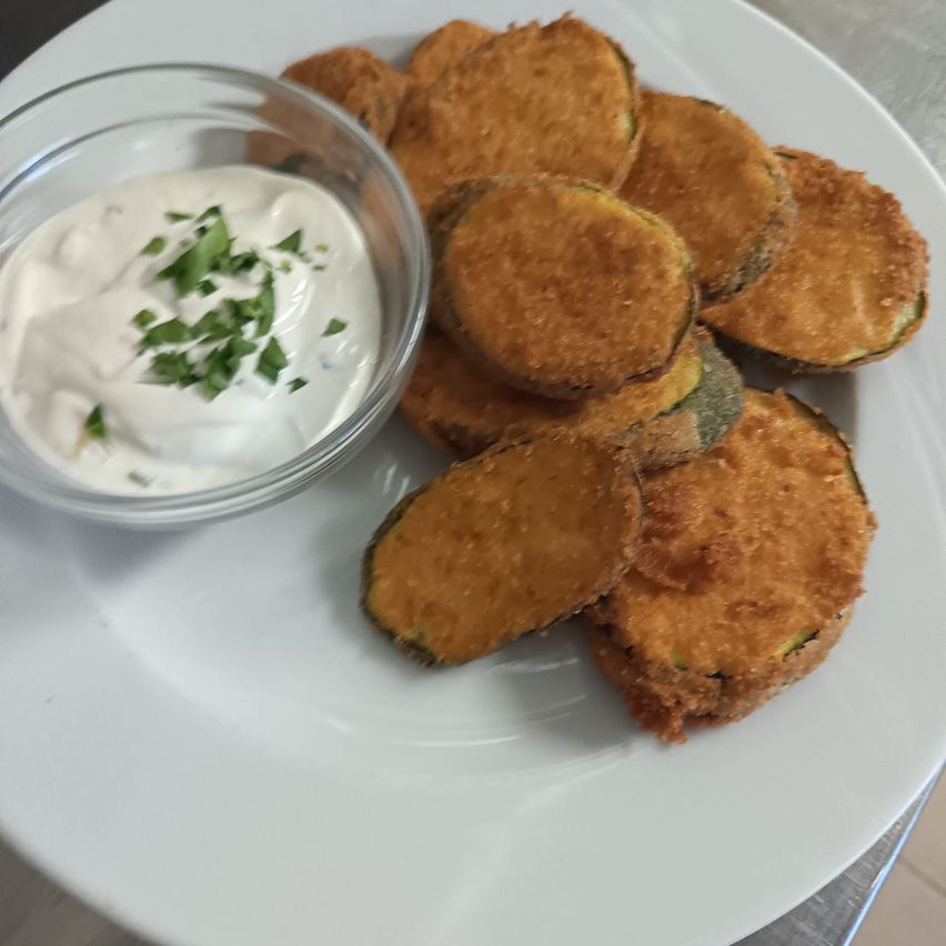 Ein Teller mit frittierten Zucchinischeiben und einer Schüssel mit cremiger Dip-Beilage.