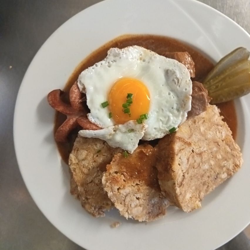 Ein Teller mit traditionellem deutschem Essen, bestehend aus einem gebratenen Ei, Wurst und Brot, serviert mit einer Beilage aus Essiggurken und Soße.
