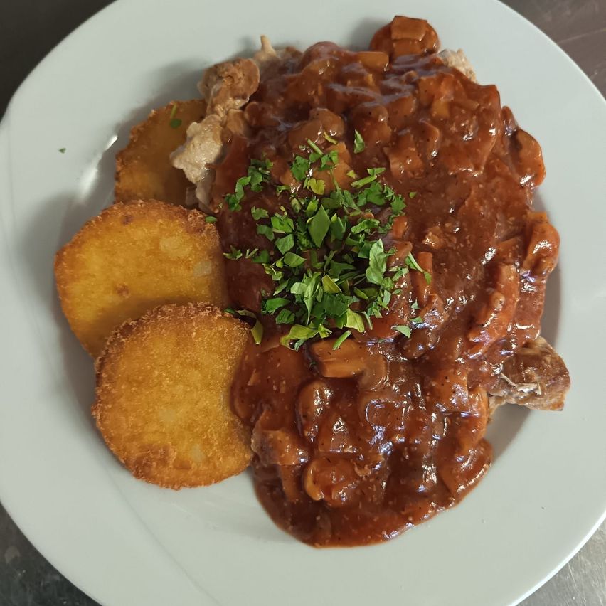 A plate of braised meat with gravy, accompanied by two golden potato dumplings, garnished with green herbs.