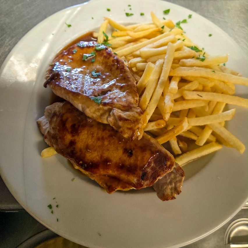 Ein Teller mit zwei Stücken glasiertem Hähnchen, garniert mit Petersilie und einer Beilage goldener Pommes frites.