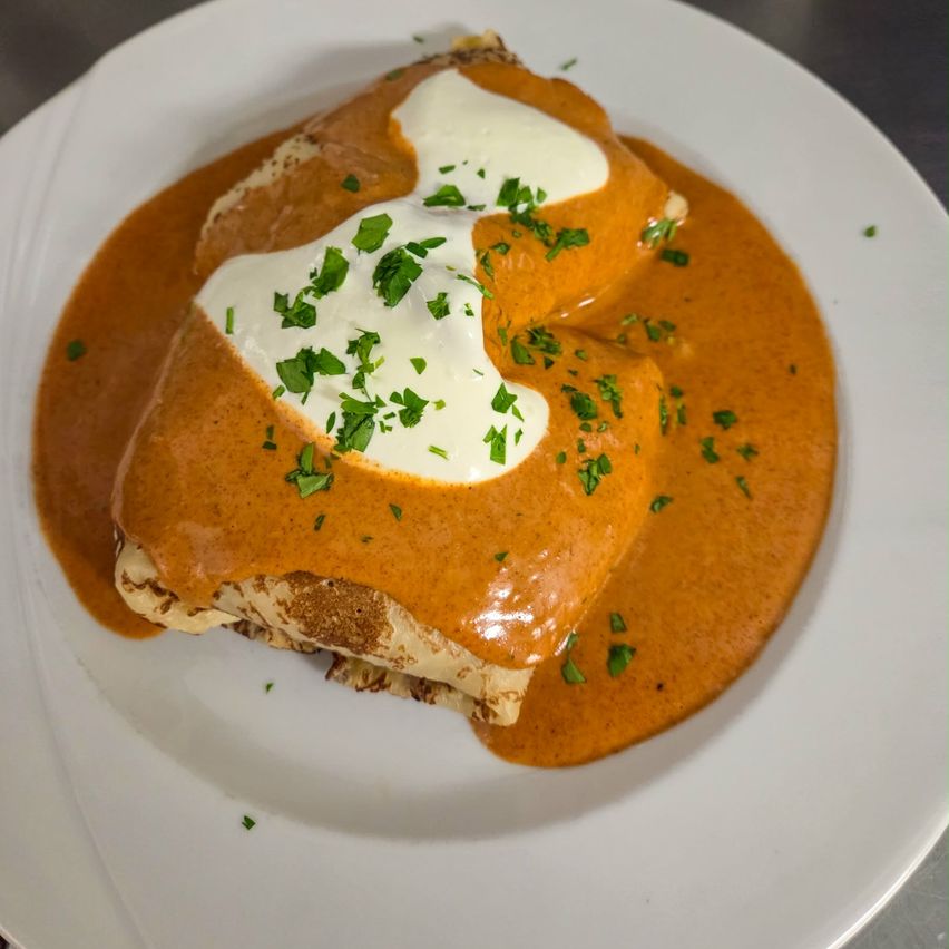 Ein Gericht mit weißer und brauner Sauce und Petersiliengarnitur auf einem weißen Teller. Das Gericht ist wie eine Enchilada gefaltet.