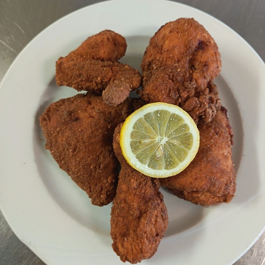 Ein Teller mit knusprigem frittiertem Hähnchen mit einer Zitronenscheibe darauf. Das Hähnchen ist goldbraun.